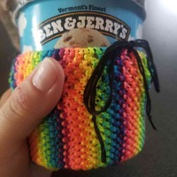 A photo of a person's hand holding a ben & jerry's peanut butter cup ice cream pint. An extremely bright, macrame woven basket is slid over it