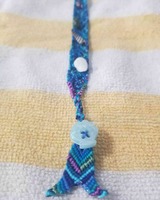 A photo of single mermaid bracelet with a blue color scheme. Small seashells are woven into the pattern and some of the knots are tied with shiny embroidery floss.