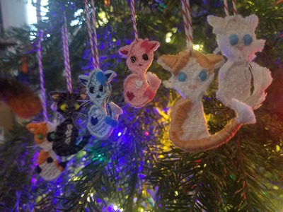 A photo of six woven cat ornaments with different coat colors hanging on a christmas tree.
