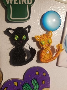 2 cat-shaped woven magnets on a fridge.