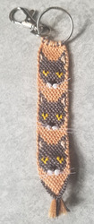 A keychain with a gray cat face with white jowls on a pale orange background