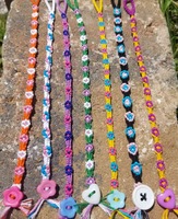 A photo of 7 pride flag themed flower chain bracelets laid out on a brick in the sunshine