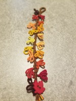 A bracelet that looks like a branch with ombre autumn leaves coming off of it moving from dark red to bright yellow