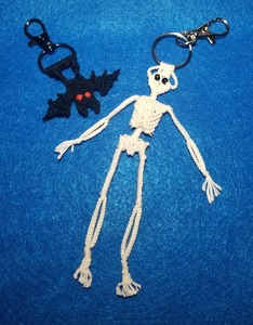 2 keychains- a small black bat with red eyes and a white skeleton with black eyes on a blue background