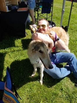 A person laying in the grass hugging a borzoi dog that is sitting on them.